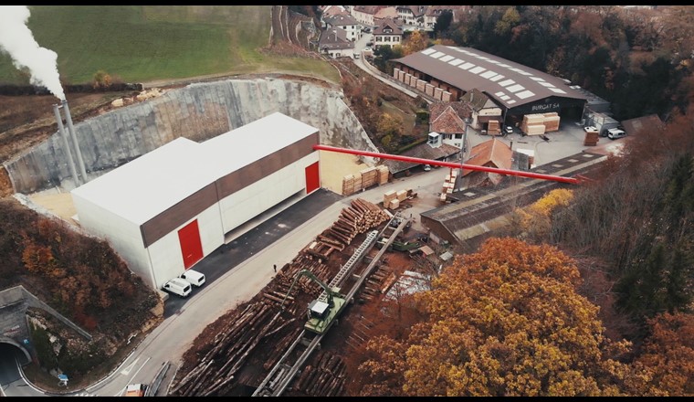 Fig. 1 Nouvelle chaufferie BéroCAD à Saint-Aubin-Sauges. Un tapis roulant aérien transporte les copeaux de bois de la scierie à la centrale thermique à bois (à gauche sur la photo). (Photo: Viteos)
