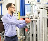 Hightech: Die Erkenntnisse aus dem neuen Reaktorkonzept dienen als Basis für den Bau von Grossanlagen: Florian Kiefer, Projektverantwortlicher für die sorptionsverstärkte Methanisierung, neben der Versuchsanlage. (Bild: ©Empa) Hightech: Die Erkenntnisse aus dem neuen Reaktorkonzept dienen als Basis für den Bau von Grossanlagen: Florian Kiefer, Projektverantwortlicher für die sorptionsverstärkte Methanisierung, neben der Versuchsanlage. (Bild: ©Empa)