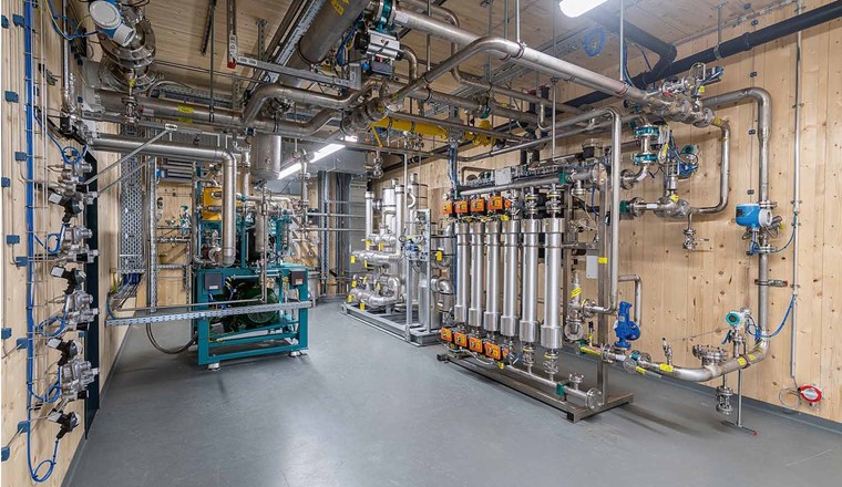 Fig. 4 Ein Verdichter (blaugrünes Aggregat) komprimiert das Klärgas auf 7 bar, bevor es in den Bioreaktor geleitet wird. Danach sorgen mehrere Aktivkohlekolonnen (Bildmitte) für die Entschwefelung des Biomethans. Die H₂-Membrane (6 Säulen) ist die letzte Reinigungsstufe vor der Einspeisung ins Gasnetz. Diese sind nötig, weil Biomethan nach bisheriger Regelung nicht mehr als 2% Wasserstoff enthalten darf. (Bild: Limeco)