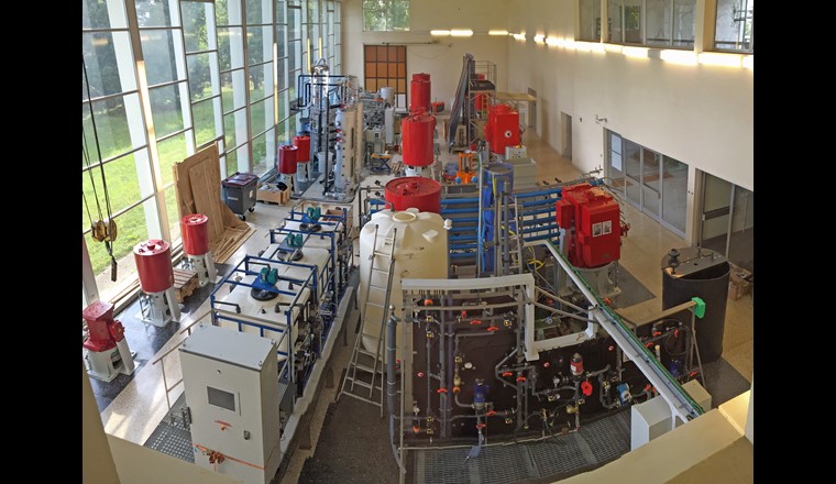 Vue des installations pilotes dans l’usine Saint-Sulpice: 1er plan droite: pilote ultrafiltration; 1er plan gauche: skid de lavage du pilote nanofiltra- tion; plan intermédiaire: pilote nanofiltration et réacteur charbon actif fluidisé  CarboPlus®; arrière-plan droite: pilote colonnes CAG; arrière-plan gauche:  pilote ozonation