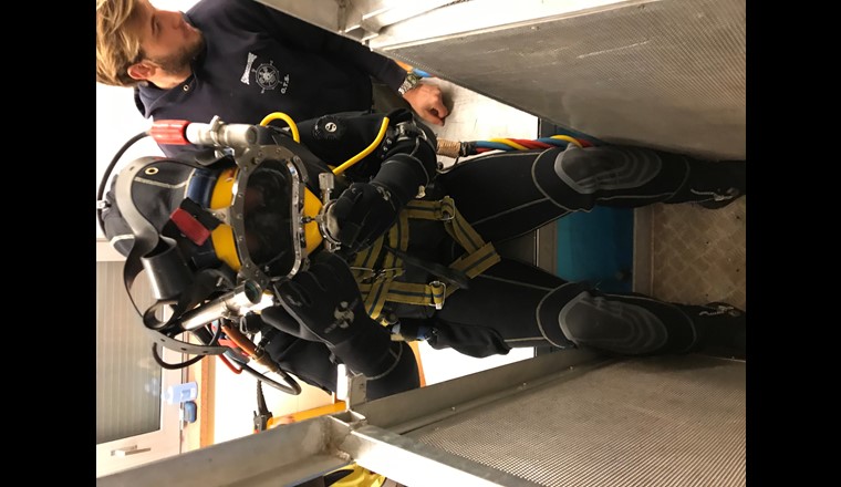 Il sub con lo scafandro si cala in acqua con una cabina