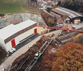 Fig. 1 Das neue Holzheizwerk des Wärmeverbunds BéroCAD in Saint-Aubin-Sauges. Ein Hängeförderband transportiert die Hackschnitzel vom Sägewerk zum Holzheizwerk (links im Bild). (Foto: Viteos) Fig. 1 Das neue Holzheizwerk des Wärmeverbunds BéroCAD in Saint-Aubin-Sauges. Ein Hängeförderband transportiert die Hackschnitzel vom Sägewerk zum Holzheizwerk (links im Bild). (Foto: Viteos)