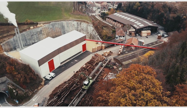 Fig. 1 Nouvelle chaufferie BéroCAD à Saint-Aubin-Sauges. Un tapis roulant aérien transporte les copeaux de bois de la scierie à la centrale thermique à bois (à gauche sur la photo). (Photo: Viteos)